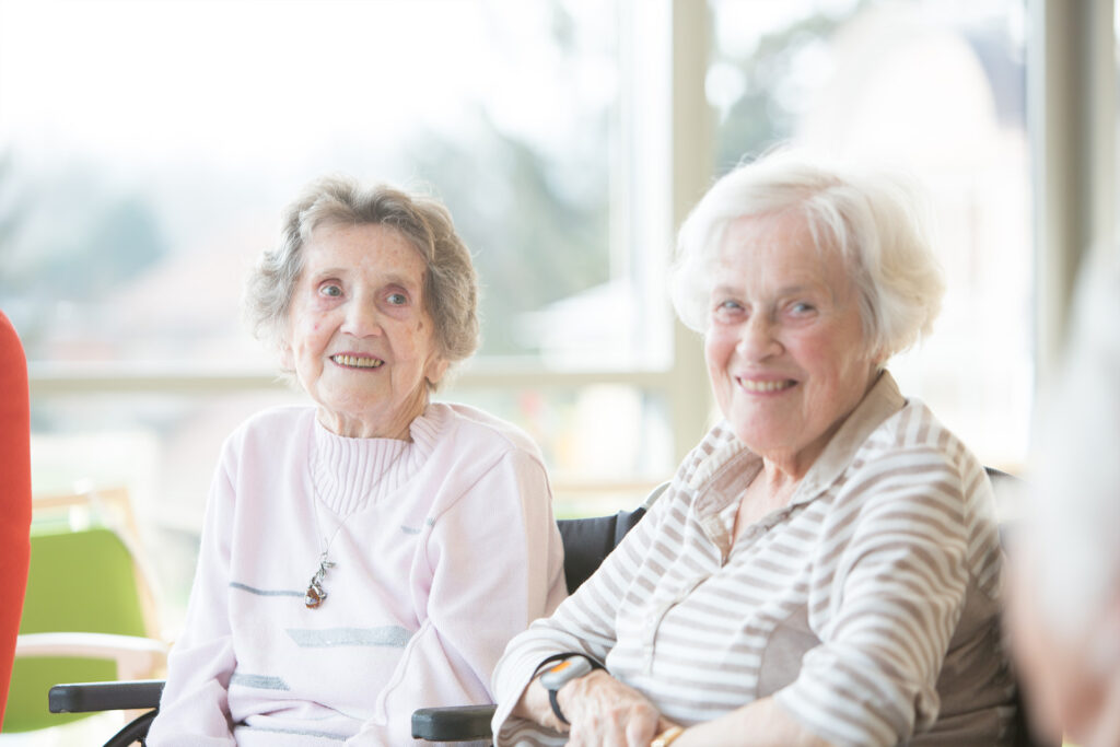 Zwei Seniorinnen sitzen fröhlich im Gemeinschaftsraum